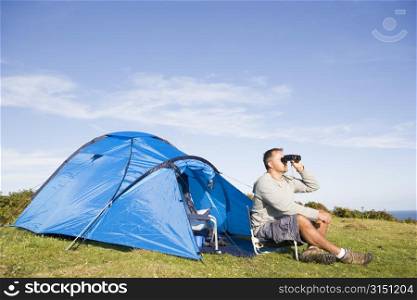 Man camping outdoors and looking through binoculars