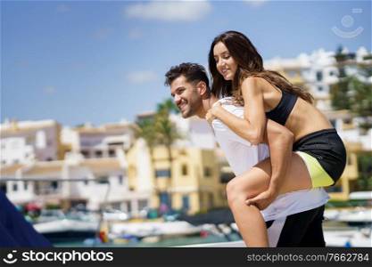 Man carrying his girlfriend on piggyback wearing sportswear.. Man carrying his girlfriend on piggyback wearing sport clothes.