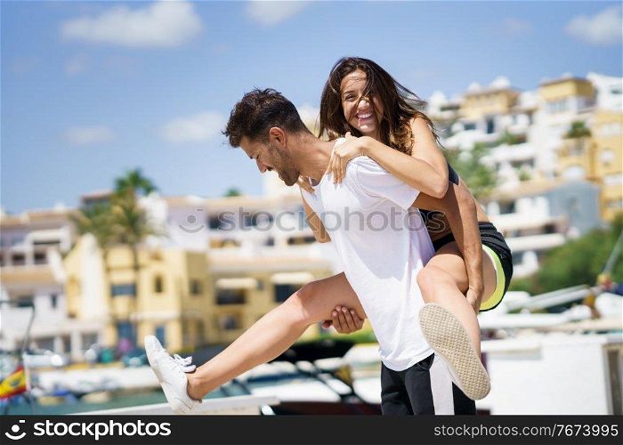 Man carrying his girlfriend on piggyback wearing sportswear. Couple having fun together.. Man carrying his girlfriend on piggyback wearing sport clothes.