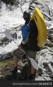 Man carrying kayak, looking at river, back view