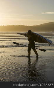 Man carrying kayak on beach at Bahobohosh Point, Makah Bay, Washington, USA