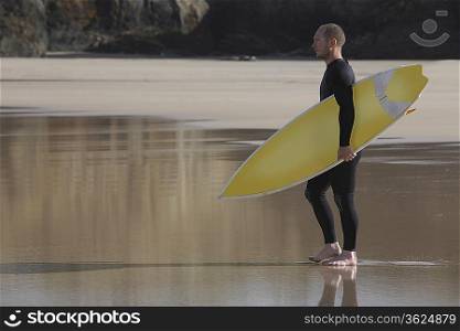 Man carrying surfboard on beach, side view