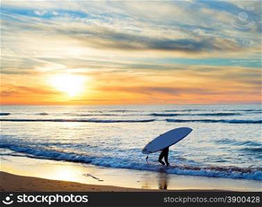 Man carrying surfboard on the beach at sunset. Sagres, Algarve region, Portugal