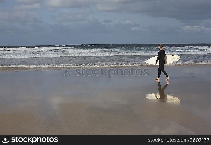 Man carrying surfboard walking on beach