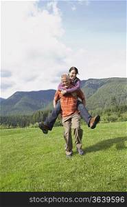Man carrying woman piggy back in meadow, laughing