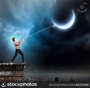 Man catching moon. Young man in casual catching moon with rope