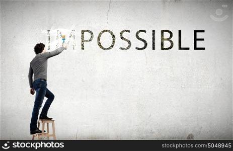 Man changing word impossible in to possible by erasing part of word with paint roller. Nothing is impossible