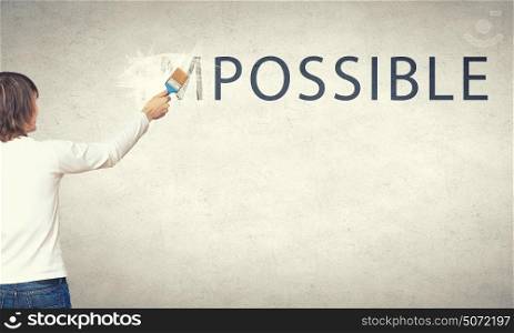 Man changing word impossible in to possible by erasing part of word with paint roller. Nothing is impossible