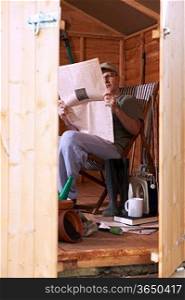 Man checking share prices while sitting in deckchair in his garden shed