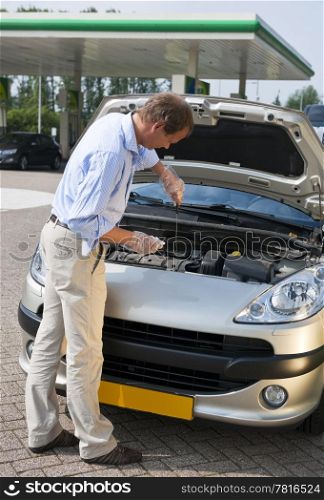 Man, checking the oil level of the engine of his car at a gas station