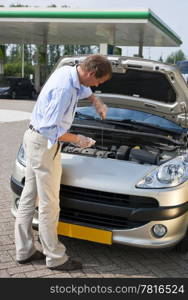 Man, checking the oil level of the engine of his car at a gas station