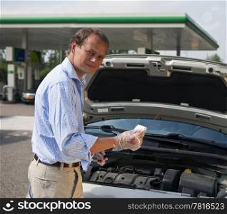 Man checking the oil levels in his car at a gas station, using a dipstick