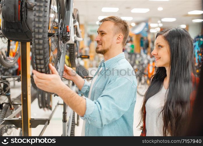 Man checks bicycle disk breaks, shopping in sports shop. Summer season extreme lifestyle, active leisure store, customers buying cycle, couple choosing bikes. Man checks bicycle disk breaks, shopping