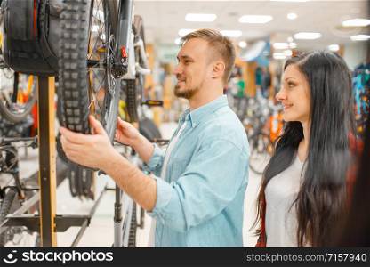 Man checks bicycle disk breaks, shopping in sports shop. Summer season extreme lifestyle, active leisure store, customers buying cycle, couple choosing bikes. Man checks bicycle disk breaks, shopping