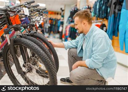 Man checks bicycle tyre, shopping in sports shop. Summer season extreme lifestyle, active leisure store, customer buying cycle equipment
