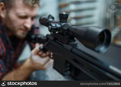 Man checks optical sight on sniper rifle in gun shop. Euqipment for hunters on stand in weapon store, hunting and sport shooting hobby. Man checks optical sight on sniper rifle, gun shop