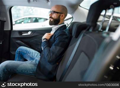 Man checks the comfort of rear seats in new automobile, car dealership. Customer in vehicle showroom, male person buying transport, auto dealer business. Man checks the comfort of rear seats in automobile