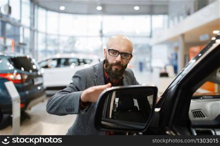 Man checks the paintwork of new pickup truck in car dealership. Customer in vehicle showroom, male person buying transport, auto dealer business. Man checks the paintwork of new pickup truck