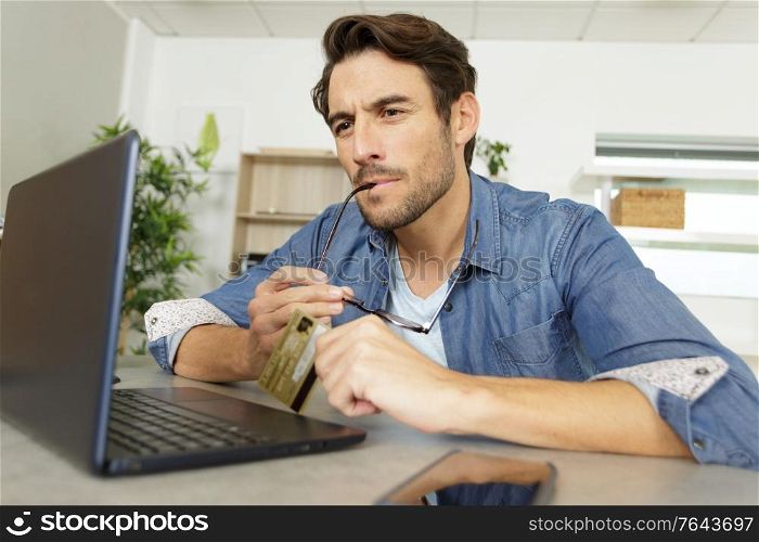 man chewing spectacles arm while making online purchase