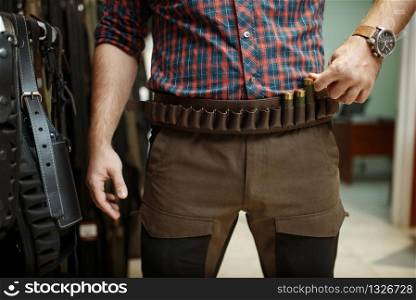 Man choosing ammo belt and uniform for hunting in gun shop. Euqipment for hunters on stand in weapon store, sport shooting hobby. Man choosing ammo belt and uniform in gun shop