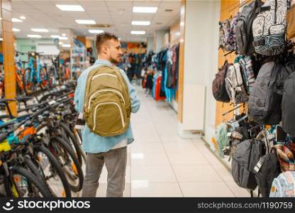 Man choosing backpack, shopping in sports shop. Summer season extreme lifestyle, active leisure store, customers buying tourist equipment