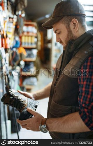 Man choosing boots for hunters at showcase in gun shop. Euqipment and rifles on stand in weapon store, hunting and sport shooting hobby. Man choosing boots for hunters in gun shop