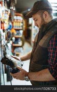 Man choosing boots for hunters at showcase in gun shop. Euqipment and rifles on stand in weapon store, hunting and sport shooting hobby. Man choosing boots for hunters in gun shop