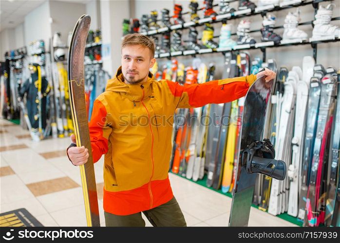 Man choosing downhill ski and snowboard, shopping in sports shop. Winter season extreme lifestyle, active leisure store, customers buying skiing equipment. Man choosing downhill ski and snowboard, shopping