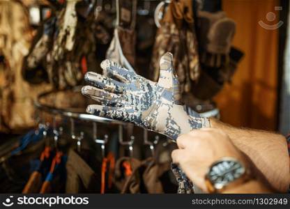 Man choosing gloves for hunters on showcase in gun shop. Euqipment and rifles on stand in weapon store, hunting and sport shooting hobby. Man choosing gloves for hunters in gun shop