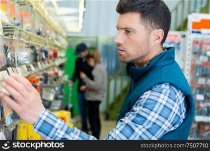 man choosing packet from display in hardware store