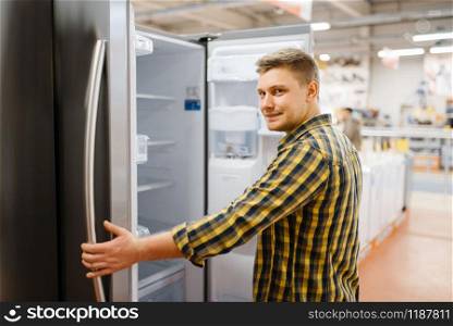 Man choosing refrigerator in electronics store. Male person buying home electrical appliances in market. Man choosing refrigerator in electronics store