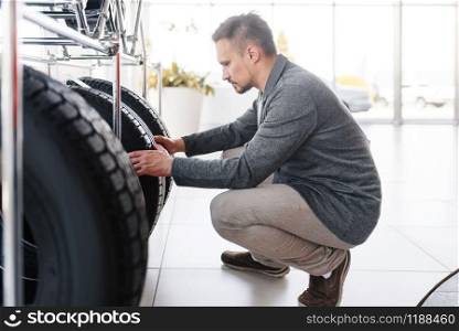Man choosing tyres for new car in showroom. Male customer buying vehicle in dealership, automobile sale, auto purchase