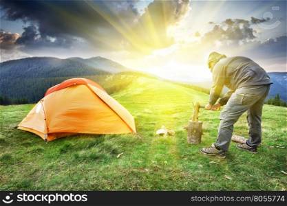 Man chopping wood near the tent in the mountains. Man chopping wood near the tent