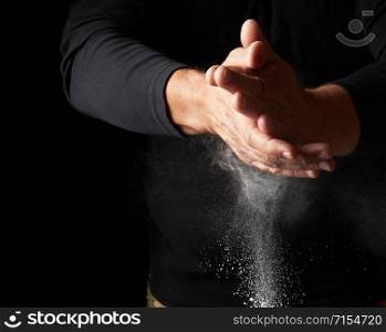 man claps his hands and scatters to the side a white substance on a black background, magnesia for rubbing hands, selective focus