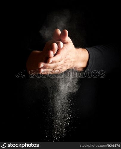 man claps his hands and scatters to the side a white substance on a black background, magnesia for rubbing hands, selective focus