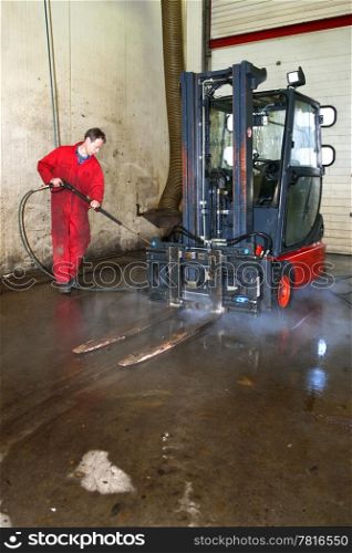 Man cleaning a forklift using a high pressure spray gun with hot, steaming, water in a workshop
