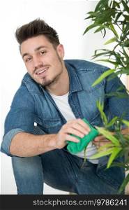 man cleaning houseplant from dust in room