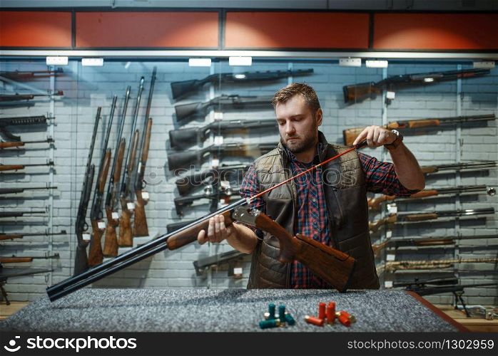 Man cleans rifle barrel at counter in gun shop. Euqipment for hunters on stand in weapon store, hunting and sport shooting hobby. Man cleans rifle barrel at counter in gun shop