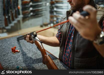 Man cleans rifle barrel at counter in gun shop. Euqipment for hunters on stand in weapon store, hunting and sport shooting hobby. Man cleans rifle barrel at counter in gun shop