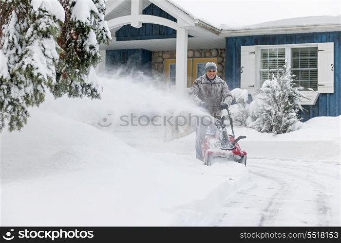 Man clearing driveway with snowblower. Man using snowblower to clear deep snow on driveway near residential house after heavy snowfall.