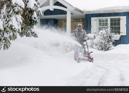 Man clearing driveway with snowblower. Man using snowblower to clear deep snow on driveway near residential house after heavy snowfall.