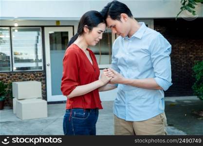 Man comforting his wife and woman hugging her husband and cry in front of the house and full of cardboard boxes during the transport in move out day, moving home concept
