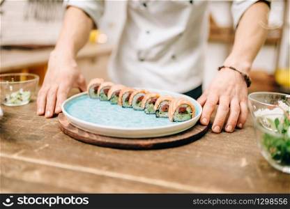 Man cooking sushi rolls on wooden table, japanese kitchen preparation process. Traditional asian cuisine, seafood delicious. Man cooking sushi rolls, japanese kitchen