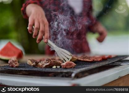 Man cooking tasty food on barbecue grill for outdoor french dinner party near the river on beautiful summer evening in nature