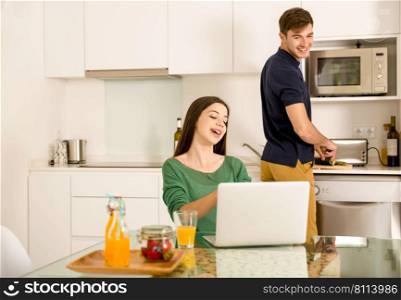 Man cooking while her wife working on a laptop