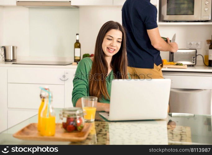 Man cooking while her wife working on a laptop