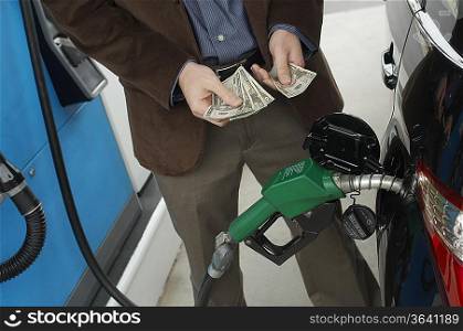 Man counting money over gas pump in car, mid section
