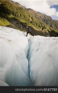 Man crosses a deep crevasse on a glacier