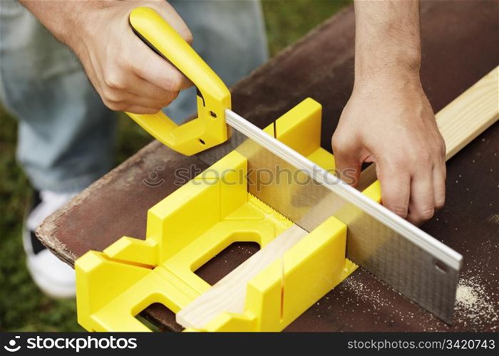 Man cutting a slat of wood using a saw and miter box outdoors.