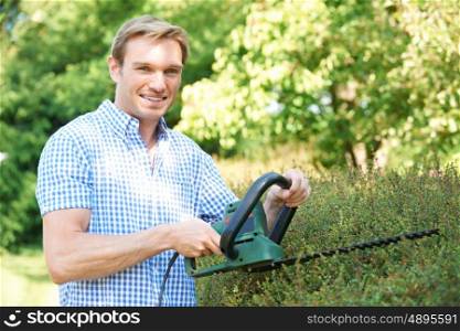 Man Cutting Garden Hedge With Electric Trimmer